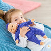 Une enfant câline son poupon Bébé Calin Capucine en robe bleue à pois sur un canapé.
