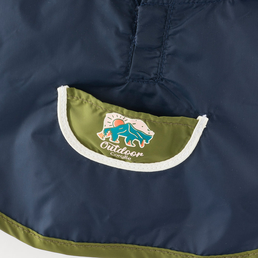 Détail du poncho de pluie petit explorateur avec logo Outdoor Corolle en tissu bleu marine.