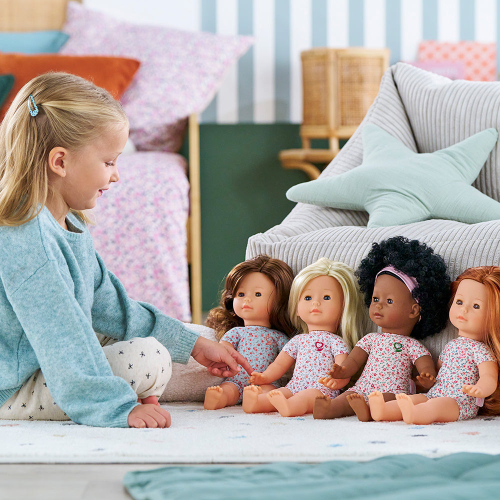 Une fille joue avec des poupées Corolle 36 cm dans un salon coloré.