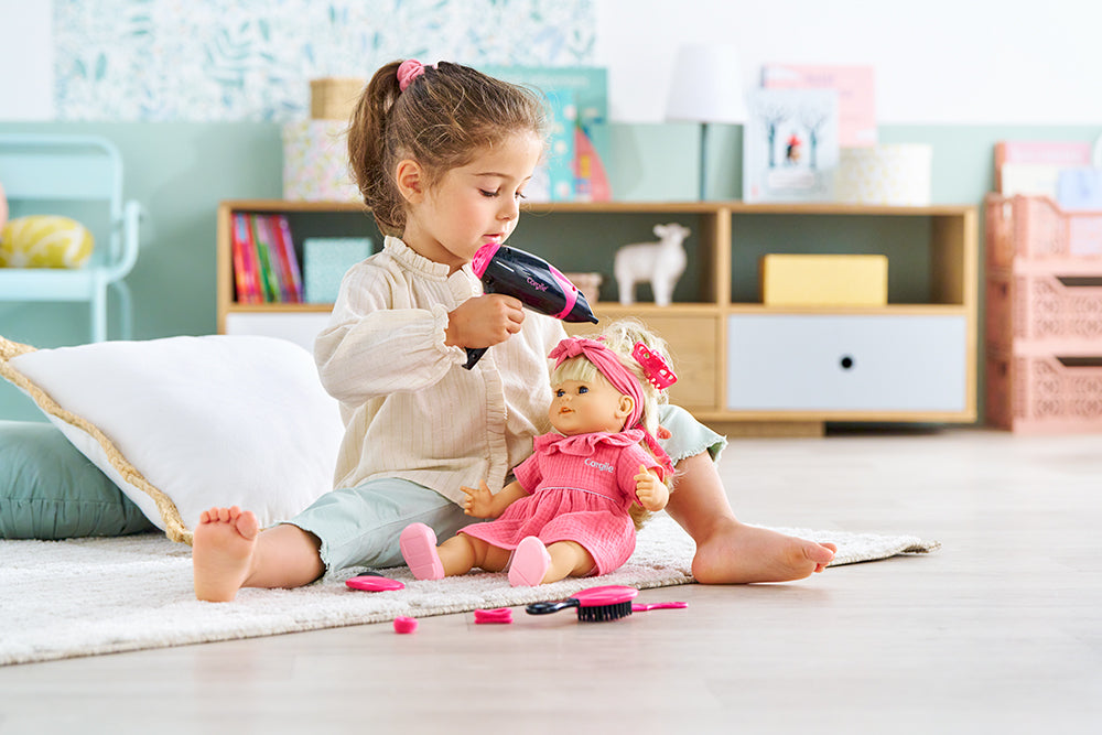 Une enfant joue avec le coffret coiffure Corolle, coiffant une poupée avec un peigne et un sèche-cheveux.