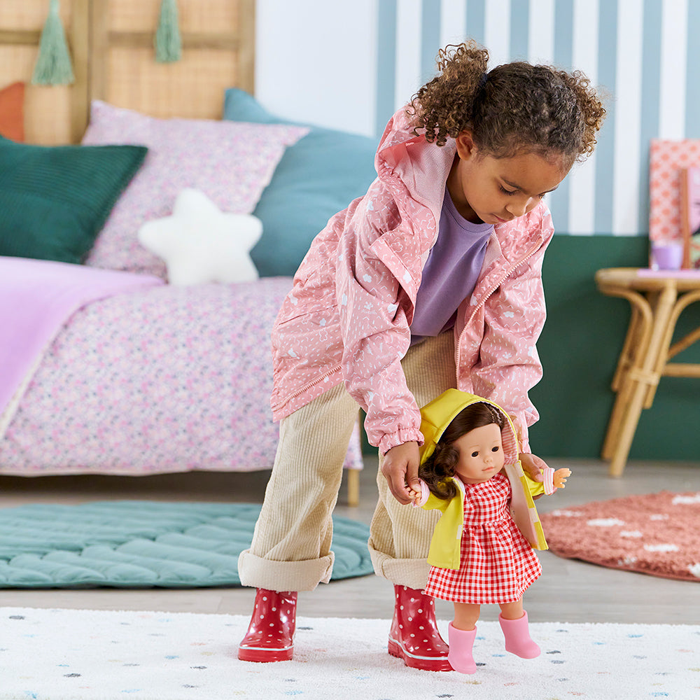 Enfant avec poupée portant des vêtements Corolle 36 cm dans une chambre colorée.