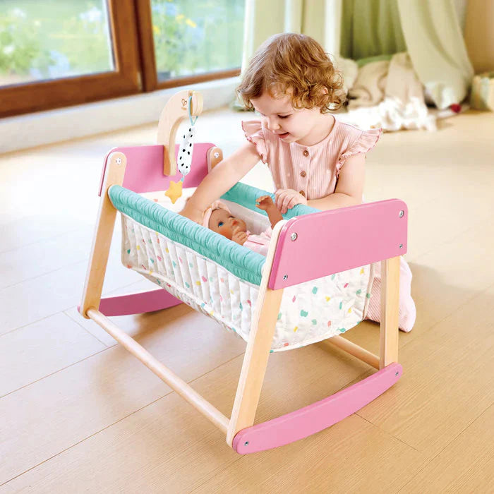 Une fille joue avec un berceau en bois pour poupée Sweet Dreams, berceau en bois pour poupée coloré en rose.