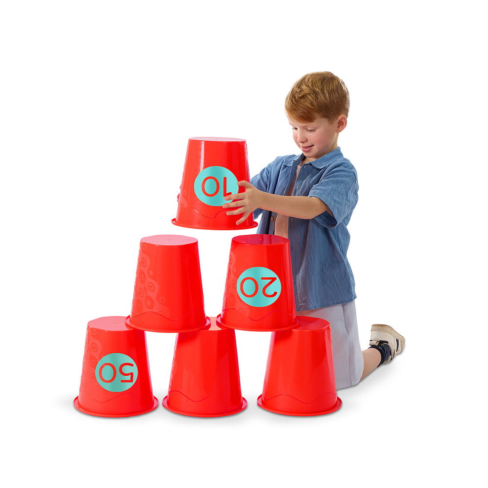 Un enfant empile des seaux emboitables pour jouer à un jeu de lancer seaux emboitables tout en s'amusant.