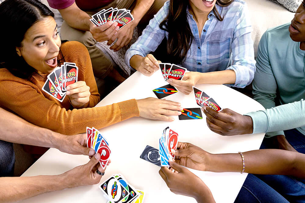 joueurs de société jouant à jeu de société UNO Party autour d'une table, cartes en main, ambiance festive