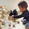 Enfant jouant avec un service à thé pour enfants thème forêt entouré de jouets en peluche et d'animaux en peluche.