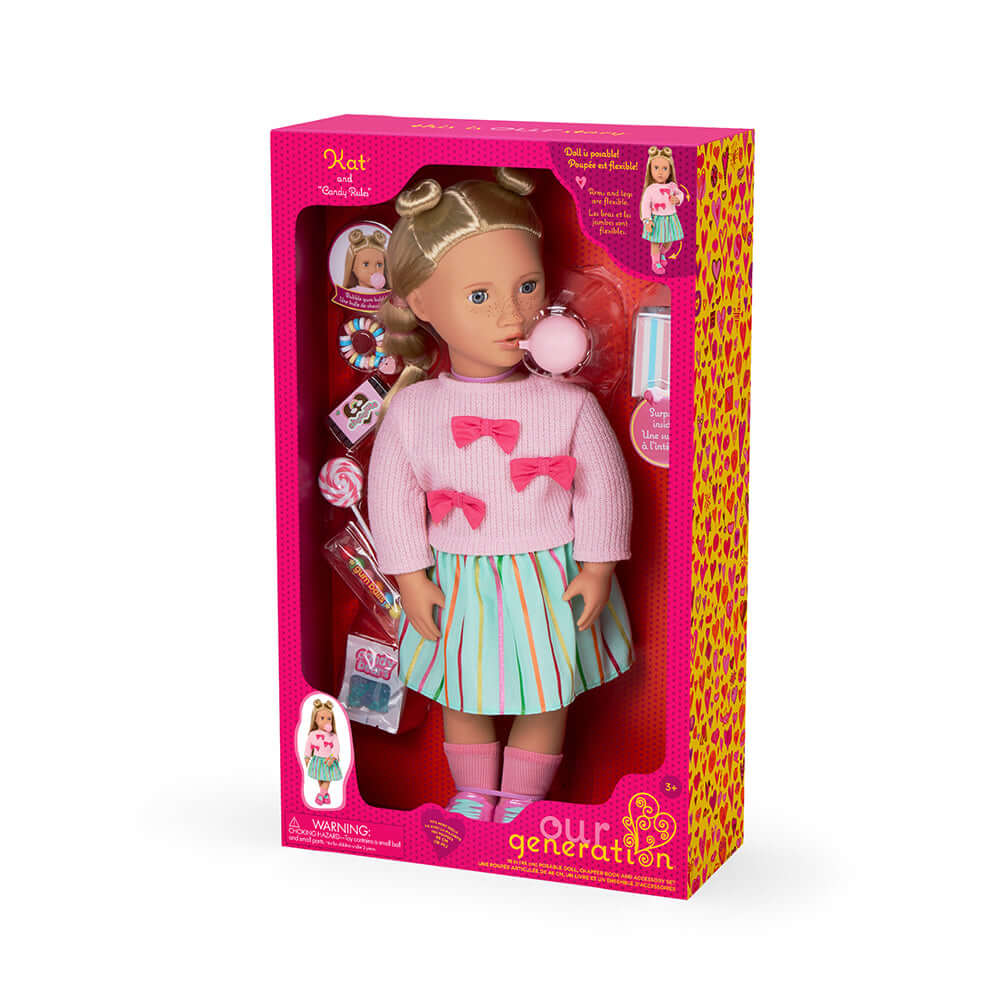 Poupée Kat Our Generation de luxe dans sa boîte, vêtue d'un pull rose et d'une jupe colorée, entourée de bonbons.