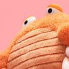 Jellycat Pinchsnap Crab en peluche avec des yeux ronds sur un fond rose.
