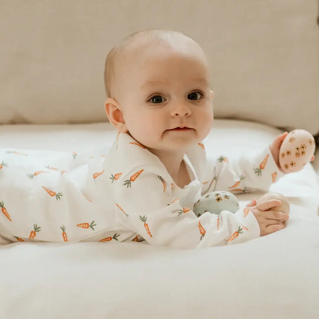 Dormeuse bébé carottes coton biologique, bébé jouant avec des œufs de Pâques, vêtue d'une dormeuse à motifs de carottes.