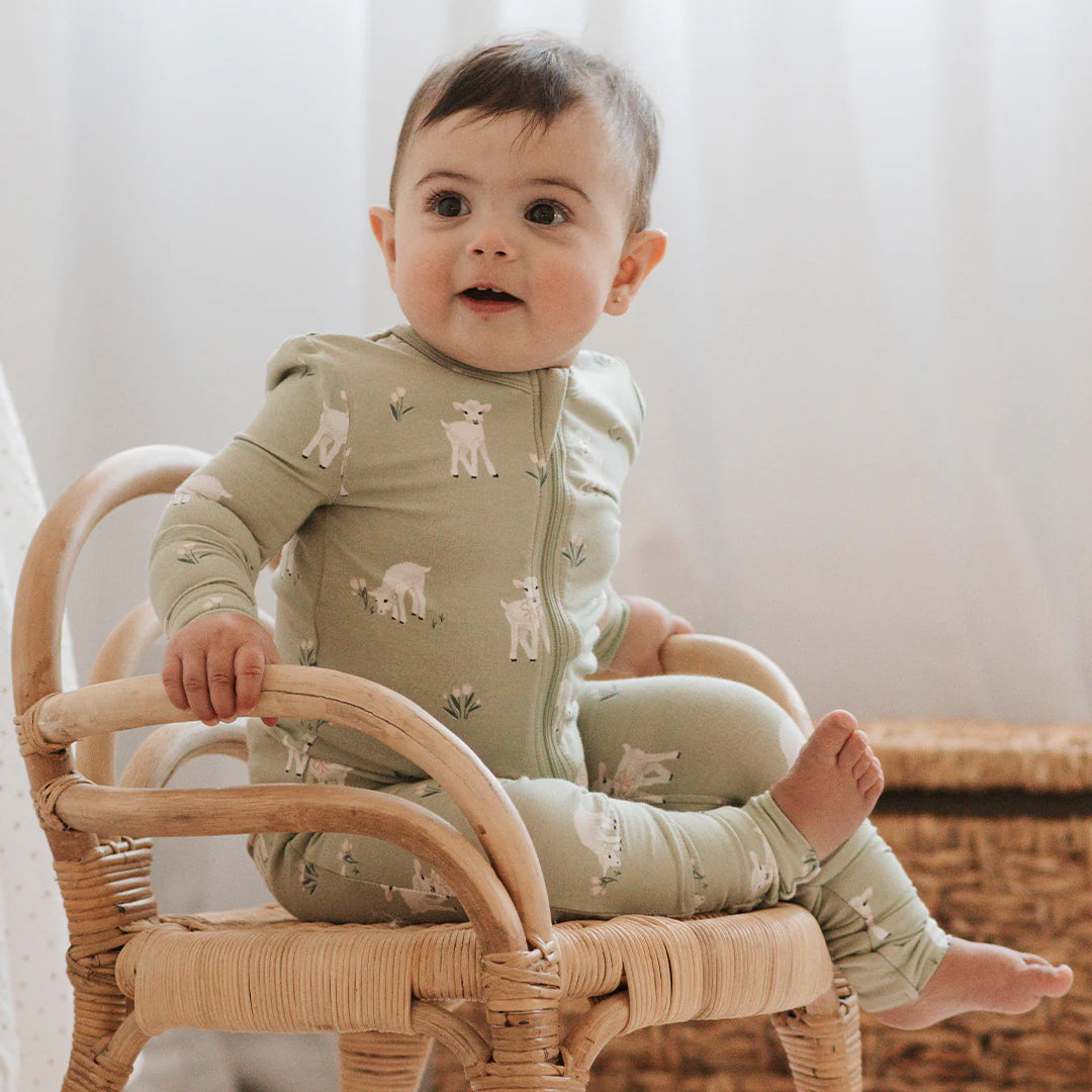 Bébé assis sur une chaise en rotin dans une dormeuse convertible bébé vert sauge avec imprimé agneaux.