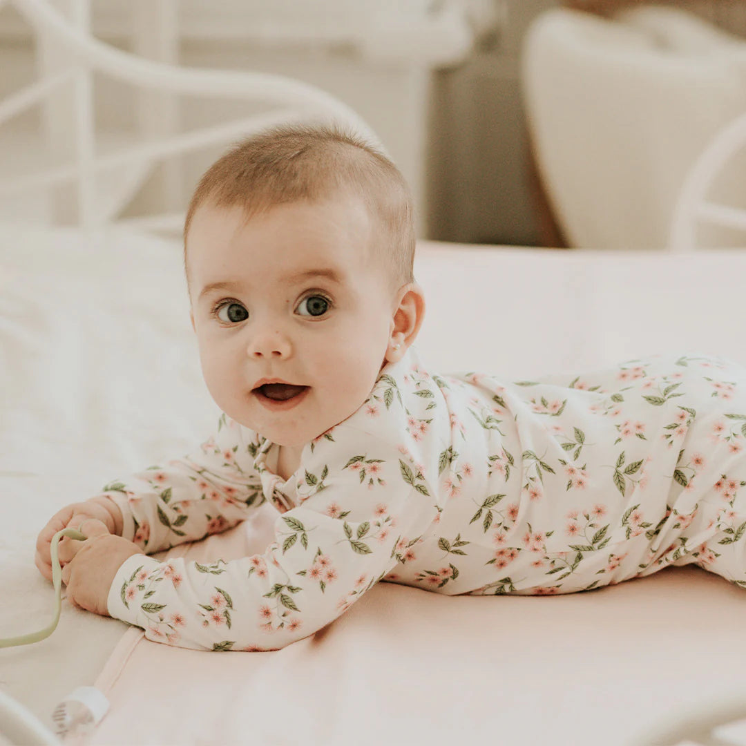 Bébé dans une dormeuse bébé primevères avec motif de fleurs sur un lit