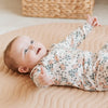 Dormeuse bébé imprimé fleurs avec motif floral sur un bébé joyeux allongé sur un tapis.