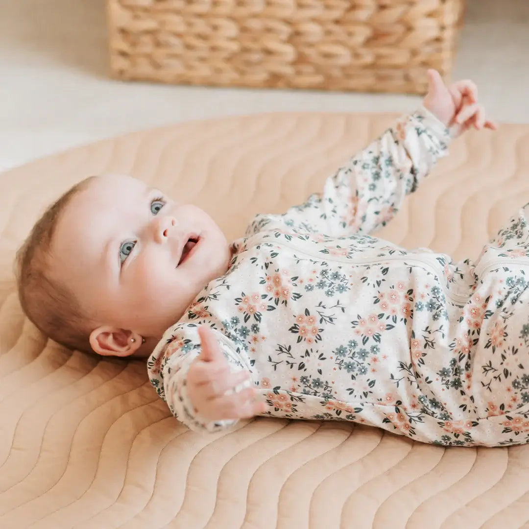 Dormeuse bébé imprimé fleurs avec motif floral sur un bébé joyeux allongé sur un tapis.