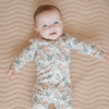 Dormeuse bébé imprimé fleurs avec un bébé souriant sur un lit beige, parfait pour les siestes.