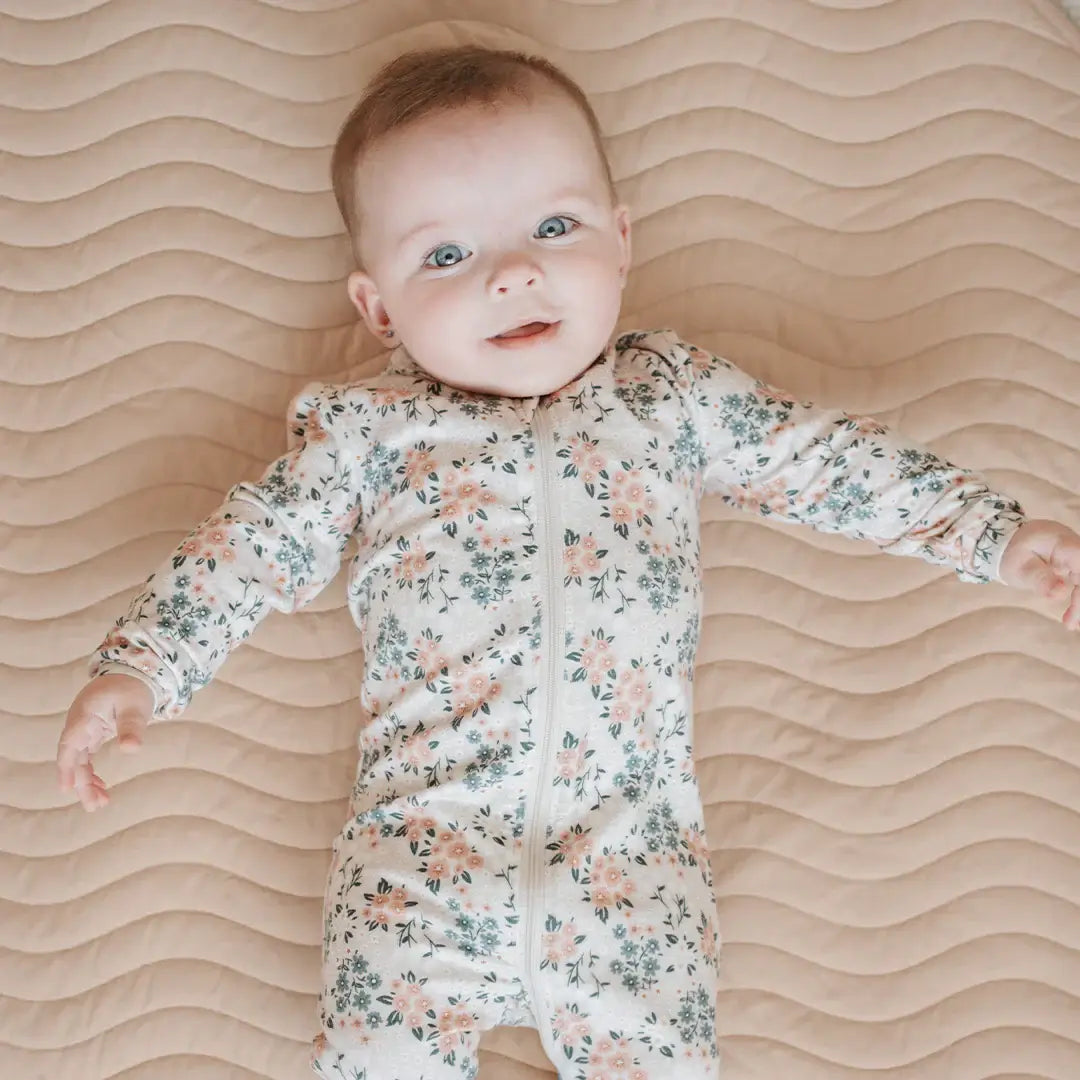 Dormeuse bébé imprimé fleurs avec un bébé souriant sur un lit beige, parfait pour les siestes.