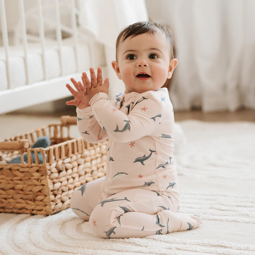 Dormeuse convertible dauphins avec un bébé souriant, assis sur un tapis, portant un pyjama à motifs de dauphins.