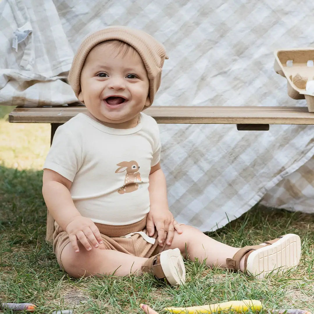 Ensemble cache-couches bébé lapins, un bébé joyeux portant un cache-couche avec un motif de lapin, assis sur l'herbe.