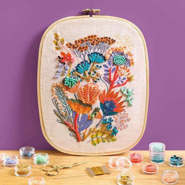 Création de perlage haute couture avec des motifs floraux colorés sur toile, devant divers perles et outils de couture.
