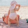 chapeau à rabat rose pâle imprimé porté par un enfant sur la plage, protégeant du soleil.