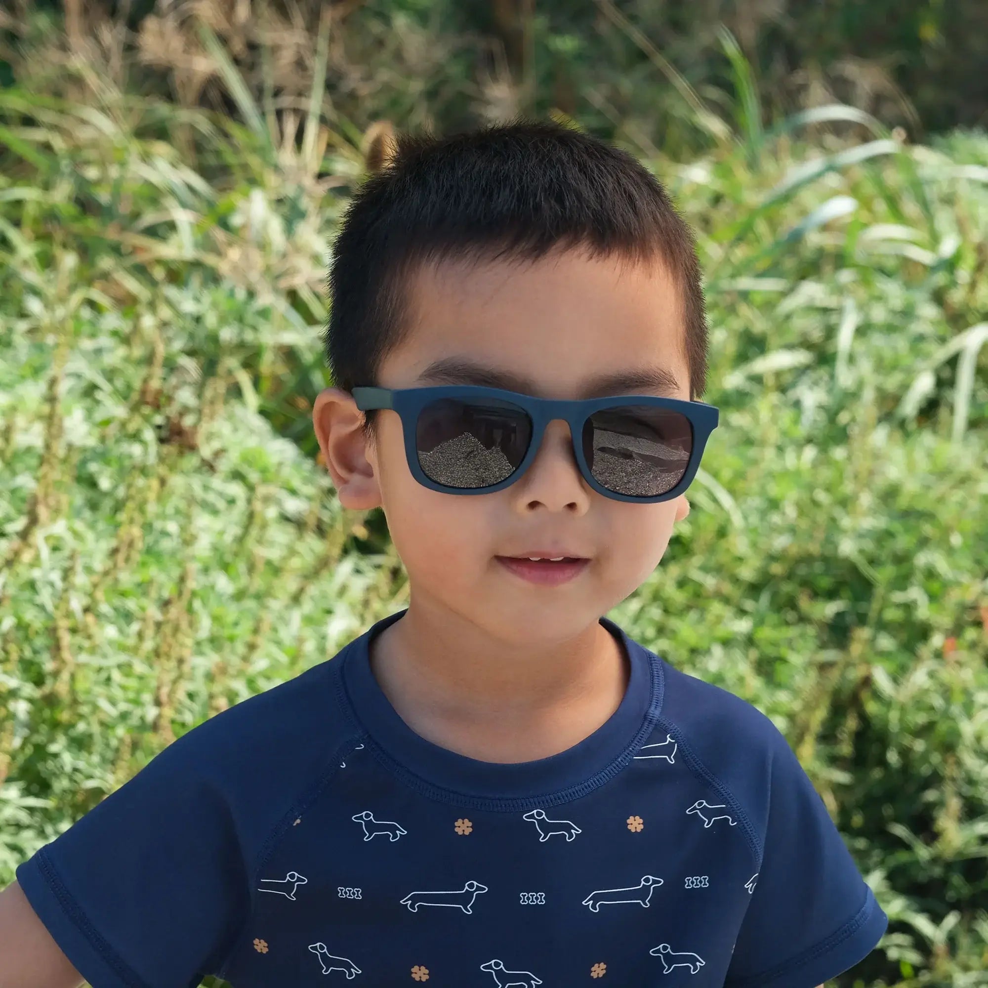 Enfant portant des lunettes de soleil urbaines Marine Foncé de Jan & Jul, devant un paysage verdoyant.